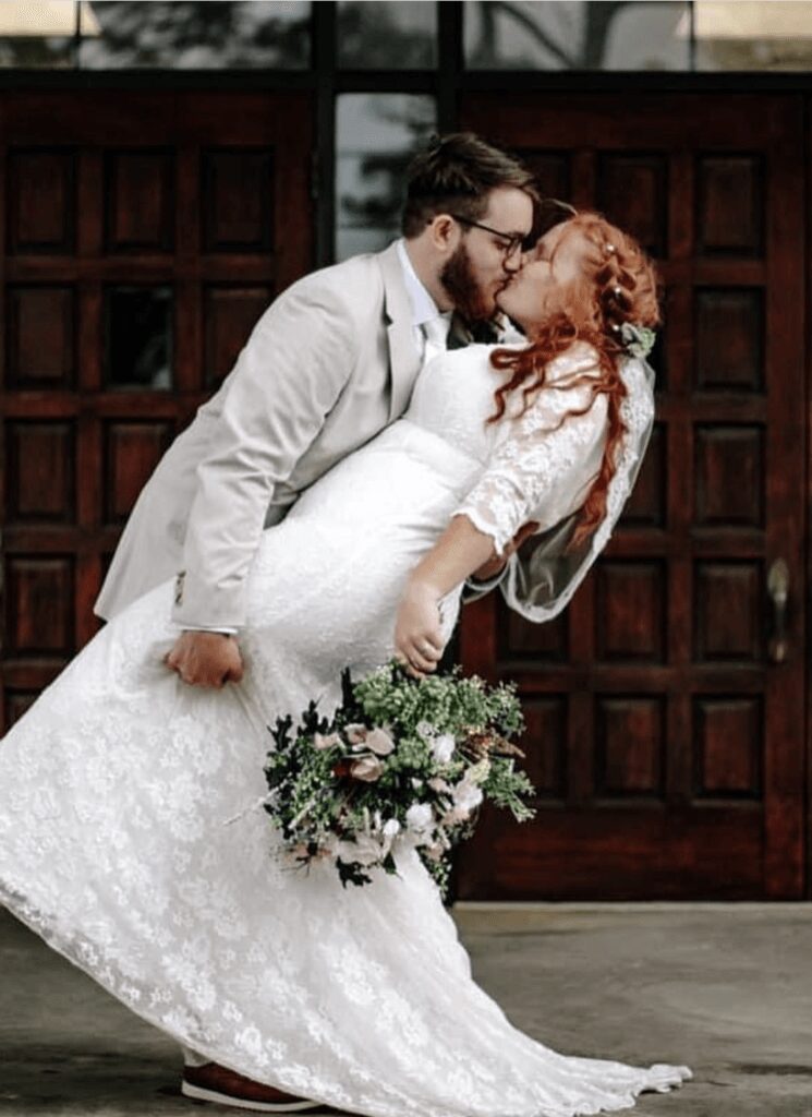 Bride and groom sharing a romantic kiss as groom dips bride in front of wooden doors.