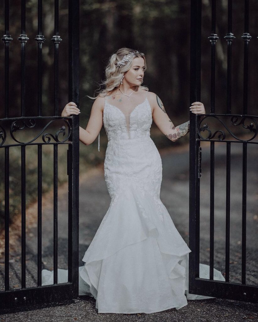 Bride in a white lace wedding dress stands gracefully outdoors.