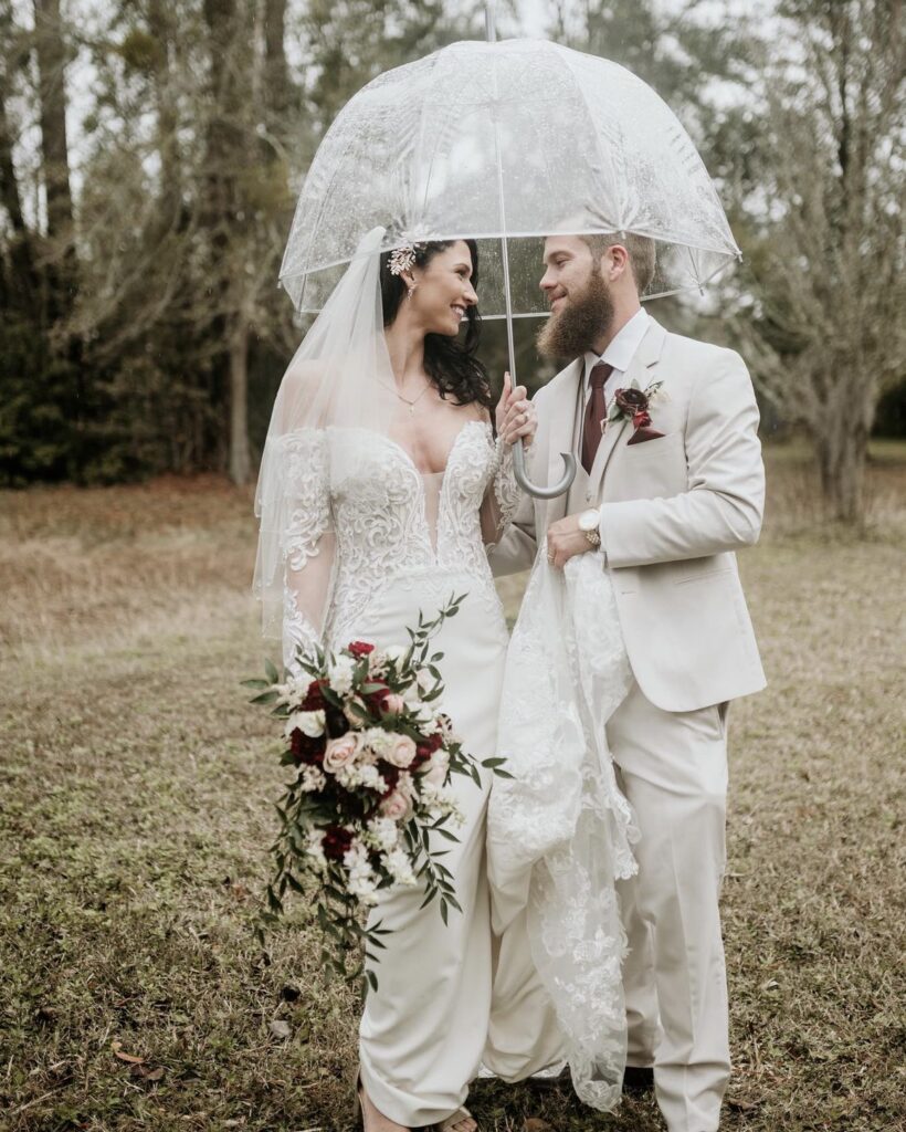 Bride and groom share a joyful moment under a lace umbrella on their wedding day.