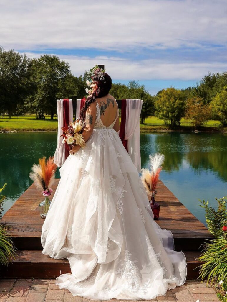 Bride in a flowing white gown with floral headpiece at outdoor wedding ceremony.