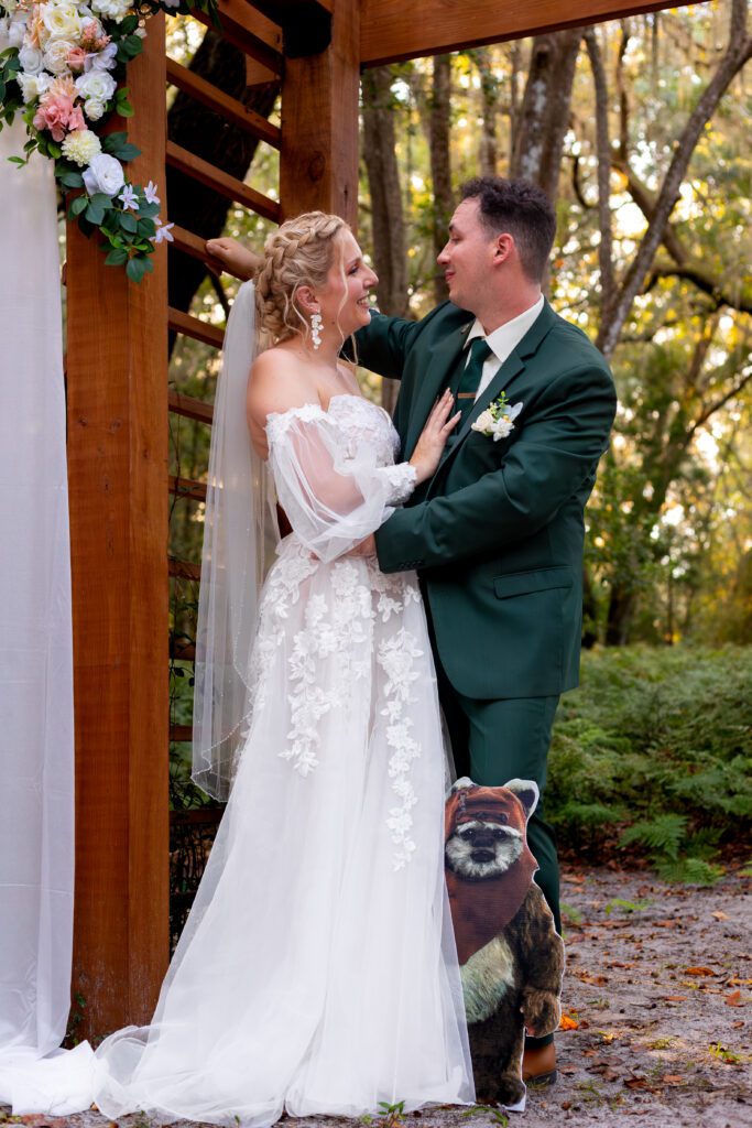 Custom Rachel Ann Bridal gown: bride in a floral applique dress with sheer sleeves and her groom in a green suit